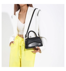 Detail of black crossbody bag featuring a wavy flap design and silver swivel metal lock