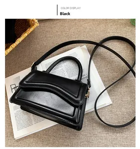 Top view of a structured black square handbag with a unique curved flap on white magazines