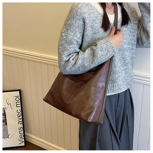 Detailed view of dark brown textured leather tote bag with wide strap on shoulder