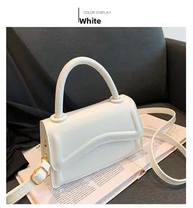 Detailed close-up of white wavy flap crossbody bag with gold hardware on fabric background