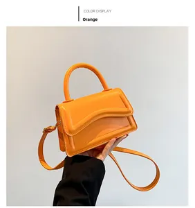 Detail of orange mini handbag with scalloped flap and golden hardware on round handle