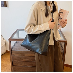 Detail of a large black leather tote bag worn by a model in a stylish commute setting