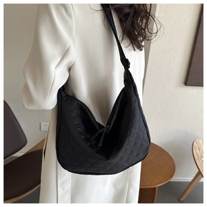 Detailed view of black quilted nylon half-moon shoulder bag on a model in a minimal room