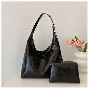 Detail of black oil-waxed leather tote and pouch set on a white table with tulips