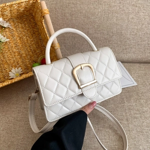 Sac bandoulière blanc matelassé avec boucle dorée et poignée dans un décor chaleureux