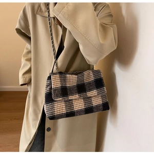 Dettaglio di borsa a tracolla in tweed a quadri con catena metallica su un trench