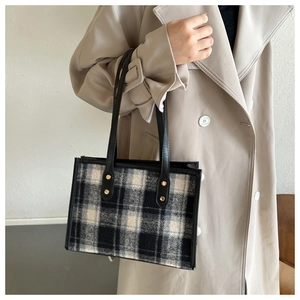 Detail der karierten Tweed-Tragetasche mit langen Ledergriffen und goldenen Metallnieten