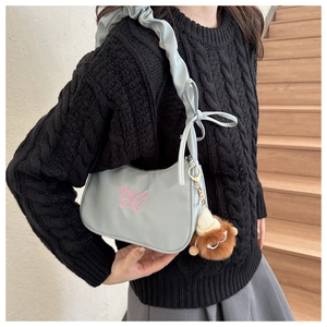 Detalle del bolso de hombro de nailon gris con bordado de mariposa y colgante de león