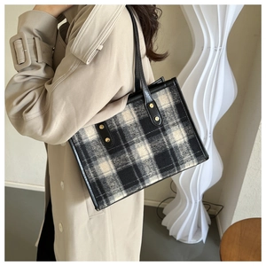Detail der Vintage-Tragetasche mit Karomuster und Lederriemen am beigen Trenchcoat