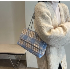 Dettaglio borsa a tracolla in tweed blu e bianco con catena su cardigan beige