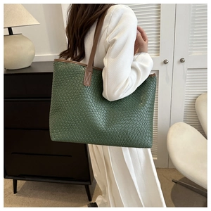 Détail d'un sac cabas vert tressé avec motifs texturés et anses d'épaule en cuir marron
