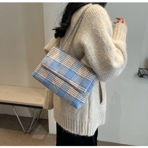 Modella che indossa una borsa a tracolla in lana a quadri blu e marrone con catena
