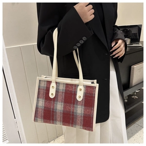 Detail der rot-grau karierten Tweed-Tasche mit cremeweißen Lederriemen und Goldnieten