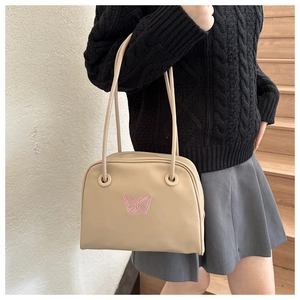 Detail of beige shoulder bag featuring pink butterfly embroidery and dual straps