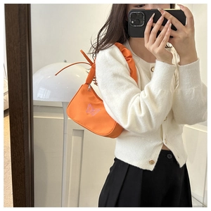 Dettaglio della borsa a spalla arancione arricciata con ricamo a farfalla rosa e texture