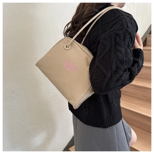 Detail of beige shoulder bag with pink butterfly embroidery on a model in sunlight