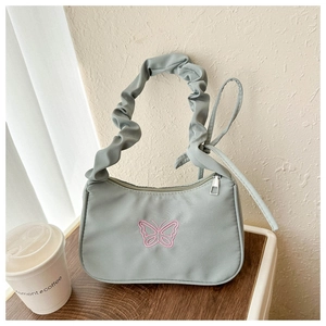 Detalle de bolso plisado azul claro con bordado de mariposa rosa sobre una mesa de madera