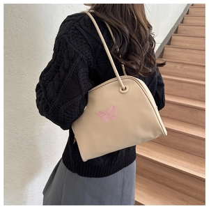 Detail of a beige shoulder bag with pink embroidered butterfly on a black sweater