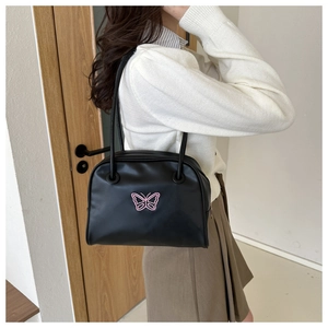 Side view of a model wearing a black shell bag with a pink butterfly embroidery detail