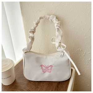 Detalle del bolso crema con bordado de mariposa rosa y correa plisada con lazo elegante