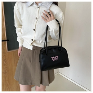 Close-up of a black leather shoulder bag featuring a stylish pink butterfly graphic pattern