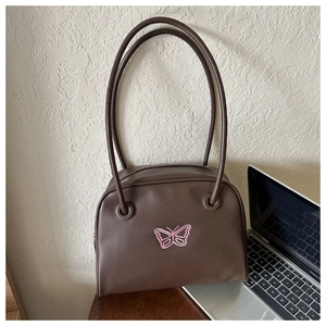 Detailed macro view of a vintage brown leather bag with delicate pink butterfly embroidery