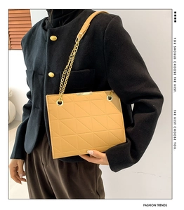 Sac fourre-tout matelassé caramel avec chaîne dorée porté sur un manteau noir