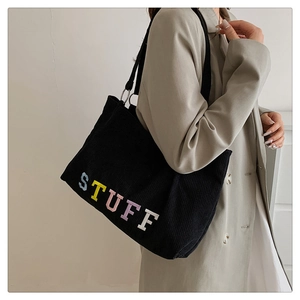 Detail of colorful STUFF embroidery on black corduroy tote bag with silver metal ring