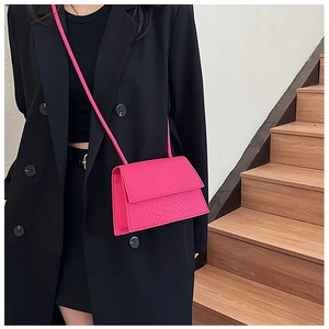 Dettaglio della borsa fucsia a tracolla effetto serpente su un blazer nero elegante