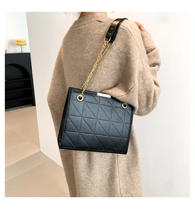 Détail d'un sac cabas noir matelassé avec chaîne dorée sur fond neutre