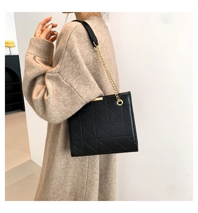 Détail du sac cabas matelassé noir avec chaîne dorée porté sur un pull en maille