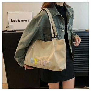 Close-up of beige corduroy tote bag with colorful STUFF embroidery and metal rings