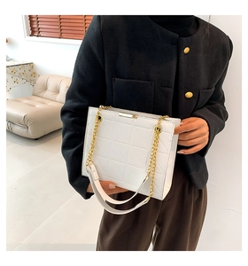 Détail d'un sac cabas blanc matelassé avec chaîne dorée porté par un mannequin chic
