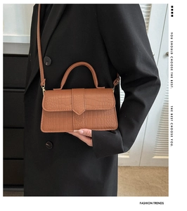 Détail de la texture crocodile marron sur le sac à rabat porté avec un blazer noir chic