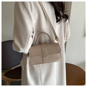 Détail du sac beige à motif crocodile avec finitions dorées posé sur une table en bois