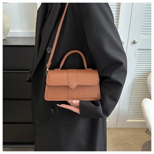 Détail du sac bandoulière marron caramel à motif crocodile porté sur un manteau noir