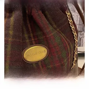 Close-up of wool plaid bucket bag with gold brand plaque and decorative metal chain