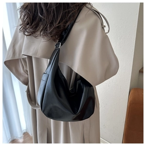 Model showing black hobo bag with shiny finish and adjustable strap over beige coat