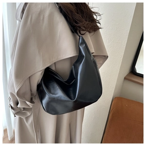 Side view of black glossy PU leather hobo bag worn with a beige trench coat for women