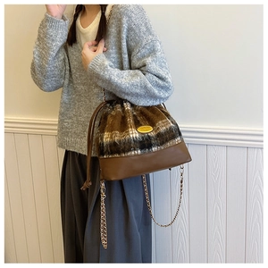Detail of wool tweed bucket bag with gold chain strap and drawstring closure on model