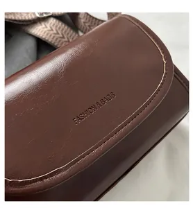 Close-up of brown glossy PU leather crossbody bag with woven strap and embossed logo