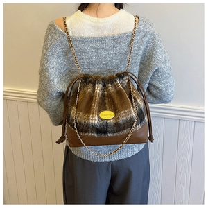Detail of wool plaid bucket bag with gold chain strap and brown leather base on a model