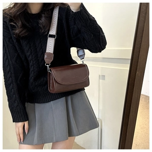 Detail of a brown leather crossbody bag with a stylish black and white woven wide strap