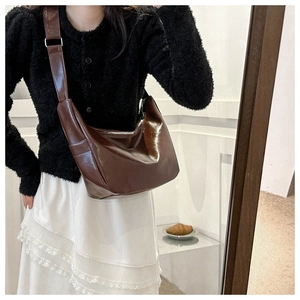 Close-up of a glossy dark brown leather hobo bag with a stylish wide adjustable shoulder strap