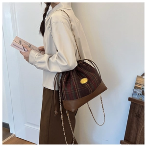 Detail of red and green tartan wool bucket bag with brown leather base and chain strap