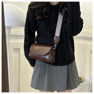 Detail of dark brown leather crossbody bag with patterned wide strap and silver hardware