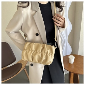 Sac nuage plissé beige porté sur un blazer clair dans un cadre urbain de café chic