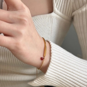 Bracelet à perles dorées avec barre incurvée et pendentif cœur rouge au poignet