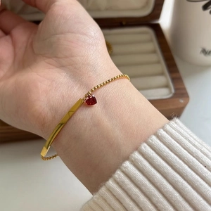 Détail du bracelet zircon cœur rouge au poignet avec perles dorées et barre