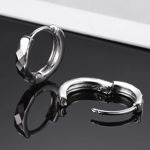 Boucles d'oreilles anneaux argentées à facettes géométriques sur fond noir brillant